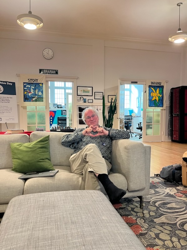 Brewster Kahle seated on a sofa, making a heart shape with his hands
