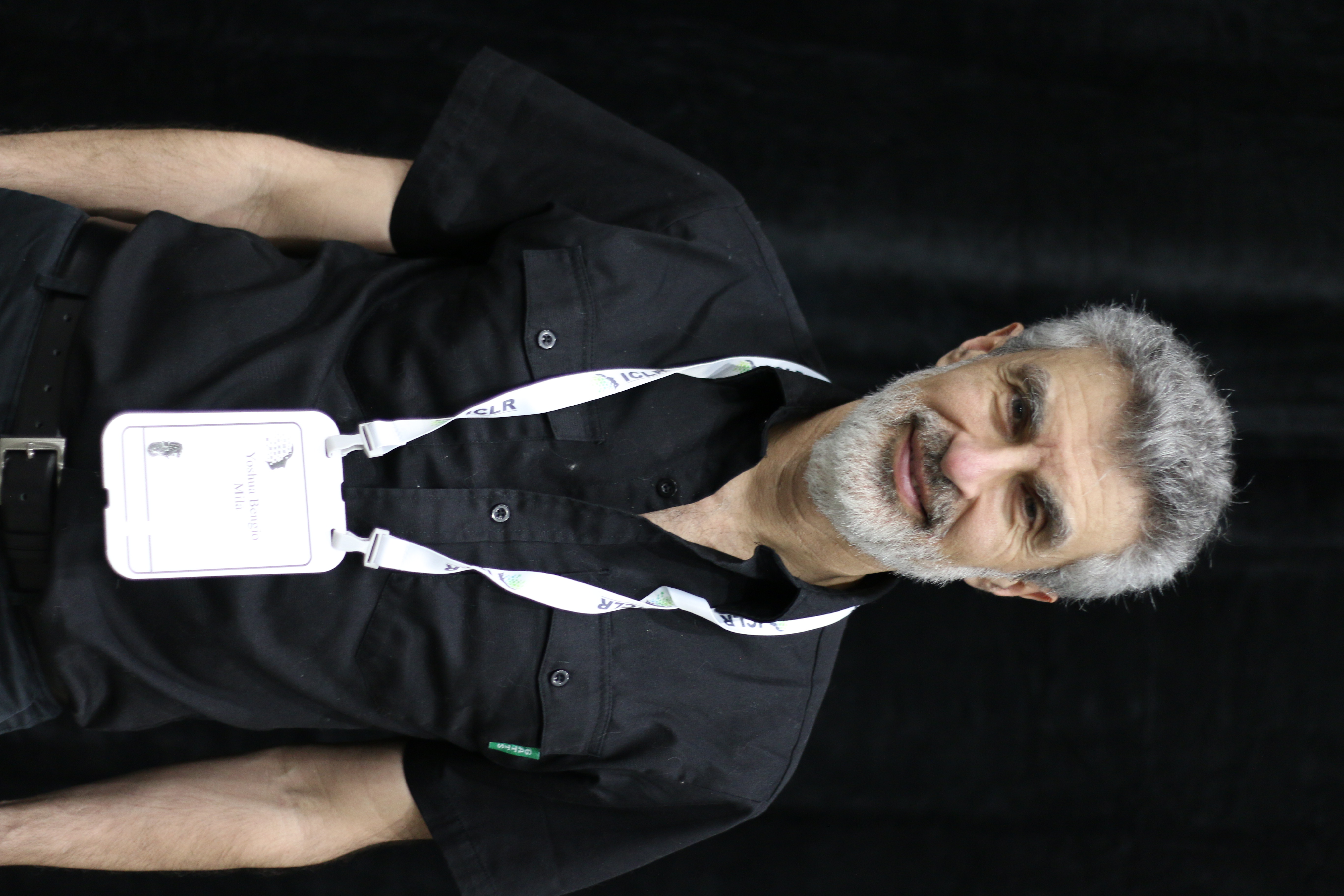 Yoshua Bengio wearing a black shirt and conference lanyard at ICLR 2025